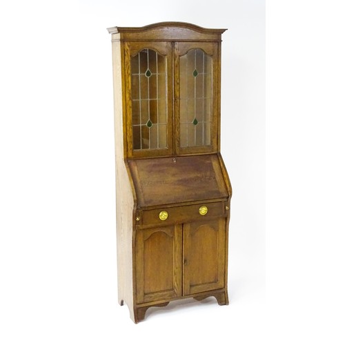 115 - An early / mid 20thC glazed oak bureau, with an arched pediment above stained, leaded glass doors, a... 