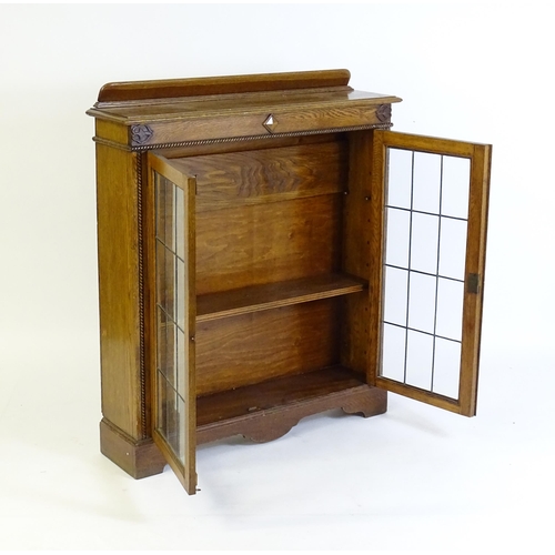 266 - A mid 20thC oak glazed bookcase with a shaped upstand above carved detailing with beadwork mouldings... 