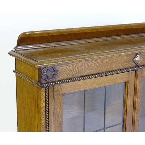 266 - A mid 20thC oak glazed bookcase with a shaped upstand above carved detailing with beadwork mouldings... 