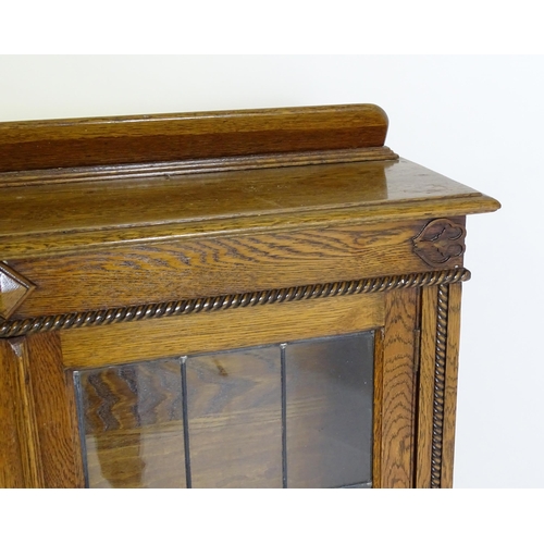 266 - A mid 20thC oak glazed bookcase with a shaped upstand above carved detailing with beadwork mouldings... 