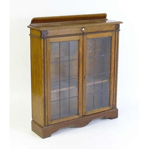 266 - A mid 20thC oak glazed bookcase with a shaped upstand above carved detailing with beadwork mouldings... 