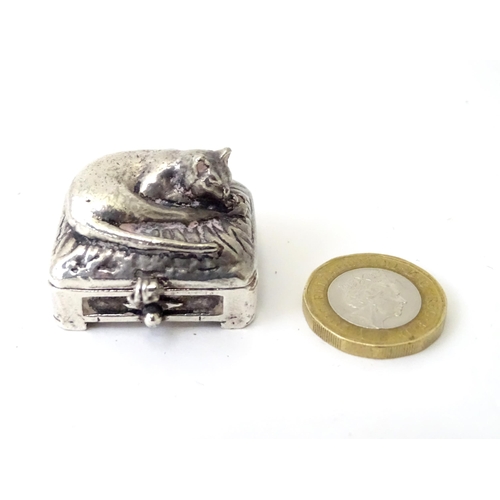 519 - A white metal pill box of oblong form surmounted by a cat. Approx. 1 3/8