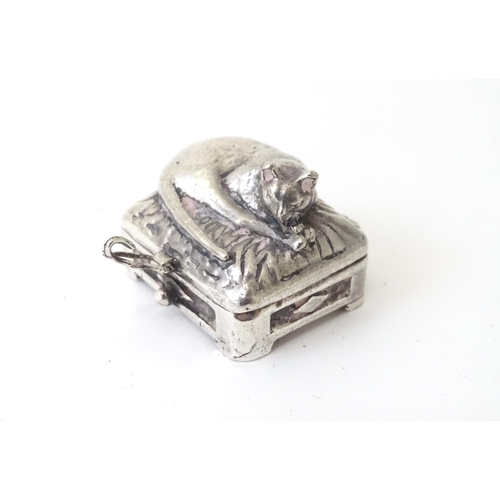 519 - A white metal pill box of oblong form surmounted by a cat. Approx. 1 3/8