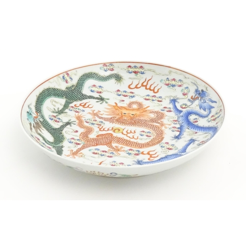 21 - A Chinese famille rose plate decorated with three dragons and a flaming pearl amongst stylised cloud... 