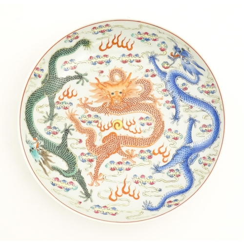 21 - A Chinese famille rose plate decorated with three dragons and a flaming pearl amongst stylised cloud... 