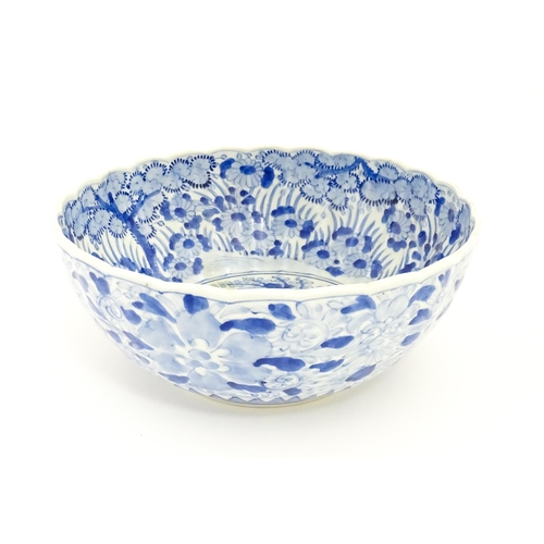 24 - A Japanese blue and white bowl with scalloped edge decorated with a central vase of flowers bordered... 