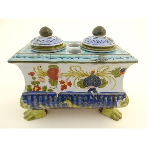 222 - A Continental faience inkwell of sarcophagus form on four paw feet with hand painted floral decorati... 