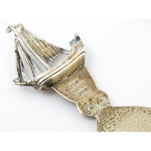 378 - An Arts & Crafts style silver caddy spoon with hammered bowl, the handle surmounted by a sailing boa... 