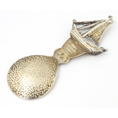 378 - An Arts & Crafts style silver caddy spoon with hammered bowl, the handle surmounted by a sailing boa... 