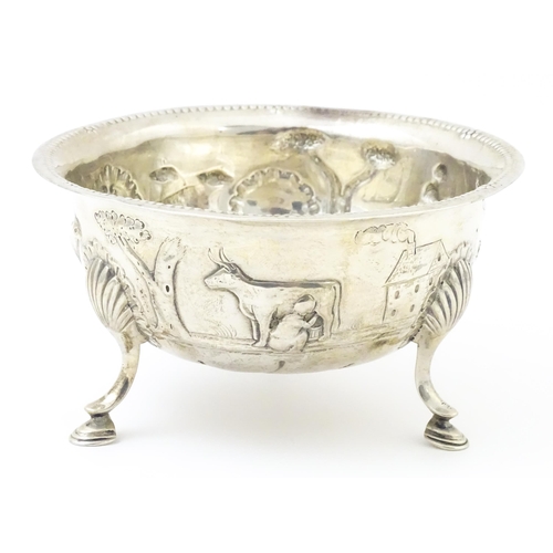 452 - An Irish silver bowl with embossed decoration depicting a cow and milkmaid, etc. raised on three fee... 