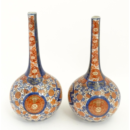 68A - A pair of Japanese bottle vases decorated in the Imari pattern with scrolling flowers and foliage. A... 