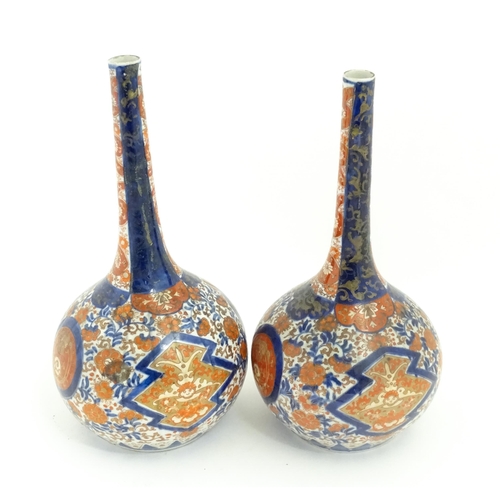 68A - A pair of Japanese bottle vases decorated in the Imari pattern with scrolling flowers and foliage. A... 