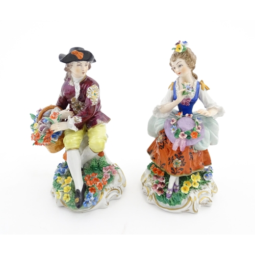 84 - A pair of Sitzendorf figures, comprising a seated male figure with a basket of flowers and seated wo... 