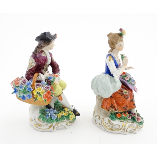 84 - A pair of Sitzendorf figures, comprising a seated male figure with a basket of flowers and seated wo... 