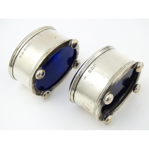 678 - A pair of silver salts of oval form with blue glass liner, hallmarked Birmingham 1921, maker H. J. C... 