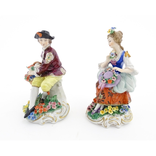 70 - A pair of Sitzendorf figures, comprising a seated male figure with a basket of flowers and seated wo... 