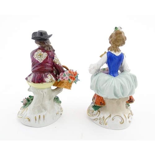 70 - A pair of Sitzendorf figures, comprising a seated male figure with a basket of flowers and seated wo... 