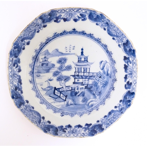 43A - A Chinese export blue and white plate depicting a river landscape scene with pagoda style buildings,... 