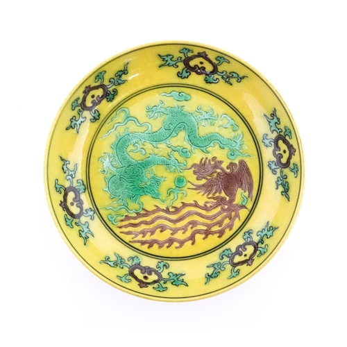 10 - A small Chinese dish with a yellow ground decorated with a dragon, phoenix and flaming pearl. Charac... 
