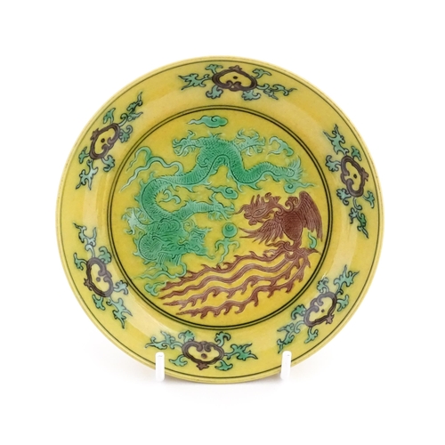 10 - A small Chinese dish with a yellow ground decorated with a dragon, phoenix and flaming pearl. Charac... 