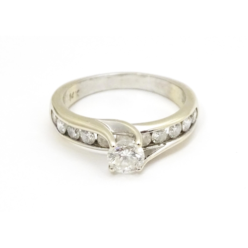 693 - A 14ct white gold ring set with a central diamond flanked by further diamonds to shoulders. Ring siz... 