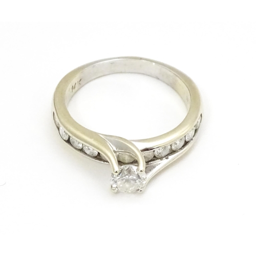 693 - A 14ct white gold ring set with a central diamond flanked by further diamonds to shoulders. Ring siz... 