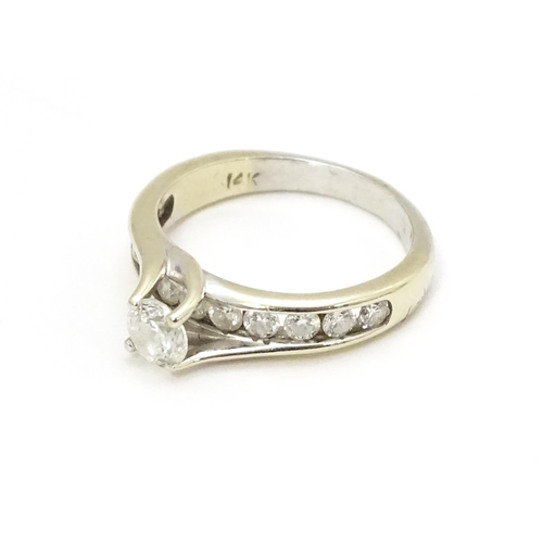 693 - A 14ct white gold ring set with a central diamond flanked by further diamonds to shoulders. Ring siz... 