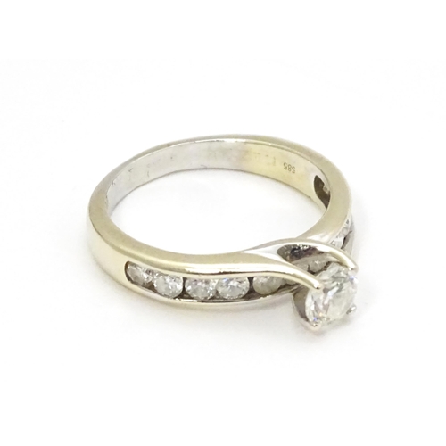 693 - A 14ct white gold ring set with a central diamond flanked by further diamonds to shoulders. Ring siz... 