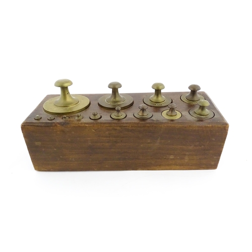 1187 - A 20thC set of 13 brass graduated weights from 2g to 2kg within a wooden block. Approx. 10 1/2