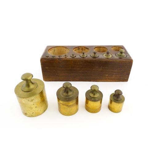 1187 - A 20thC set of 13 brass graduated weights from 2g to 2kg within a wooden block. Approx. 10 1/2