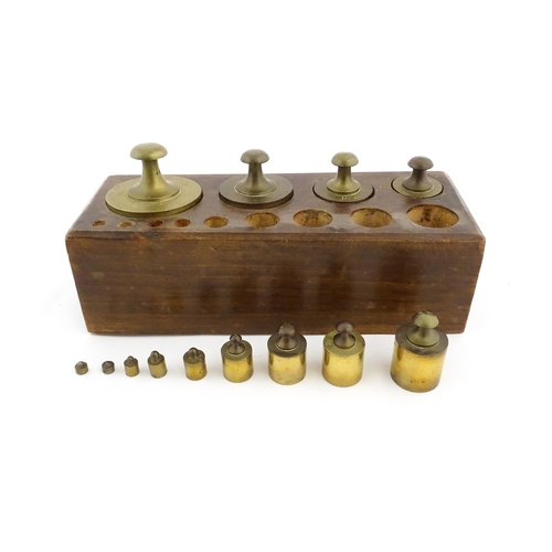 1187 - A 20thC set of 13 brass graduated weights from 2g to 2kg within a wooden block. Approx. 10 1/2