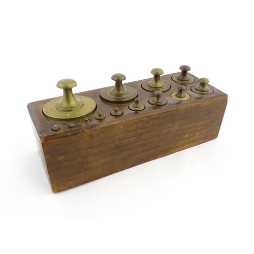 1187 - A 20thC set of 13 brass graduated weights from 2g to 2kg within a wooden block. Approx. 10 1/2