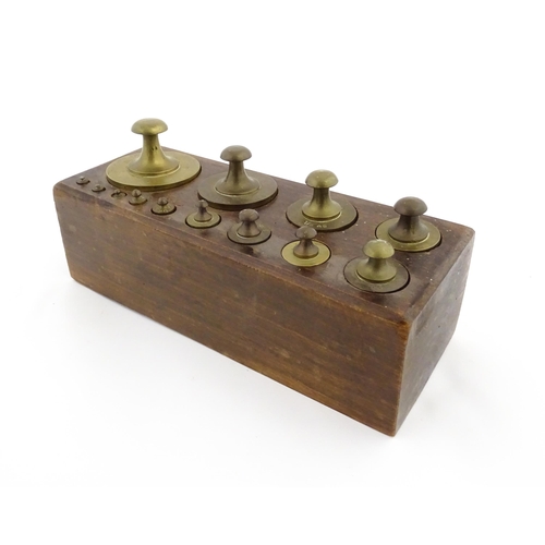 1187 - A 20thC set of 13 brass graduated weights from 2g to 2kg within a wooden block. Approx. 10 1/2