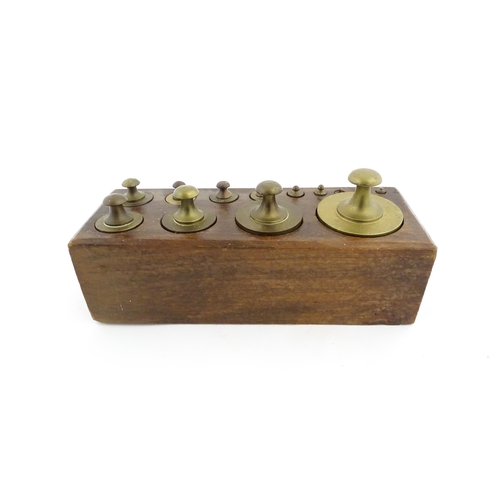 1187 - A 20thC set of 13 brass graduated weights from 2g to 2kg within a wooden block. Approx. 10 1/2