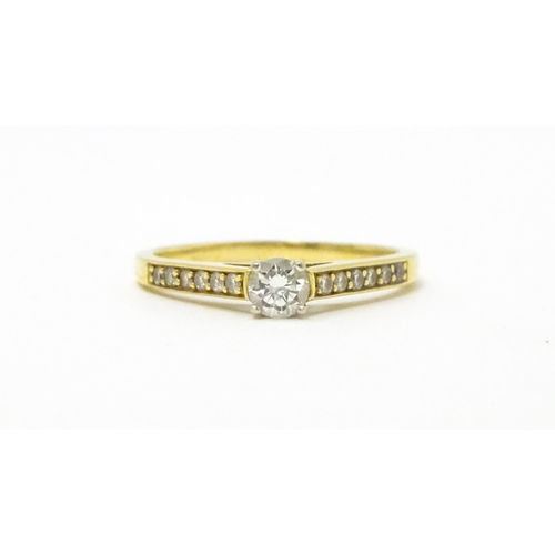 705 - An 18ct gold ring set with a central diamond flanked by further diamonds to shoulders. Ring size app... 