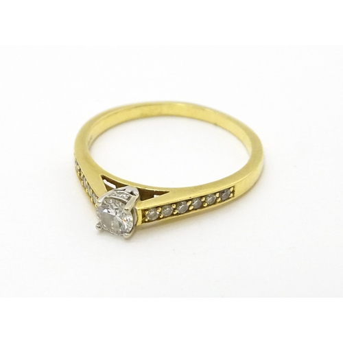 705 - An 18ct gold ring set with a central diamond flanked by further diamonds to shoulders. Ring size app... 