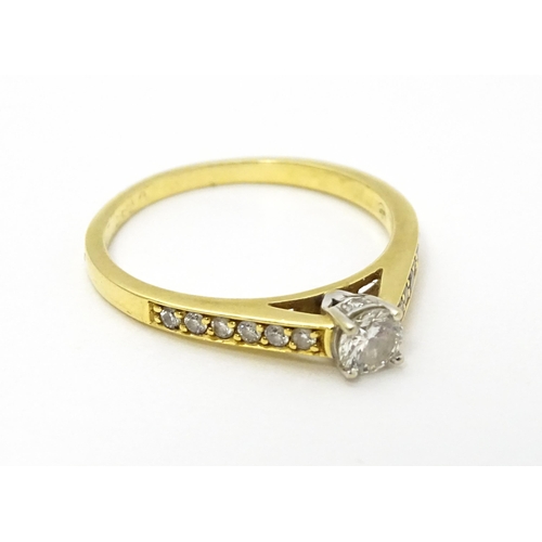 705 - An 18ct gold ring set with a central diamond flanked by further diamonds to shoulders. Ring size app... 