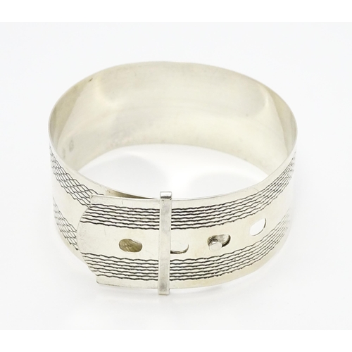 765 - A silver bangle bracelet formed as a belt with engraved decoration. Marked Sterling Silver.