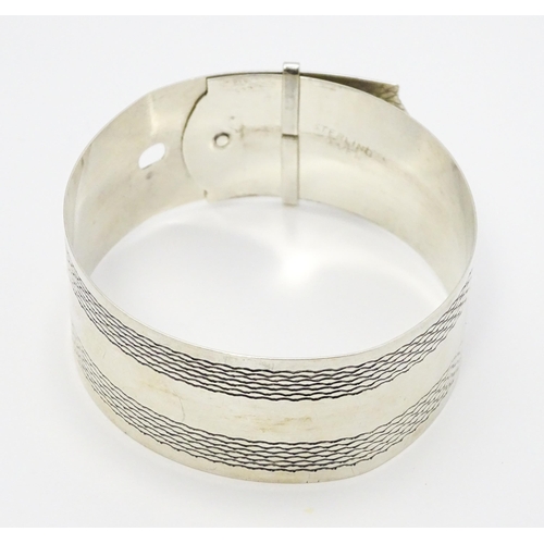 765 - A silver bangle bracelet formed as a belt with engraved decoration. Marked Sterling Silver.