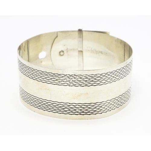 765 - A silver bangle bracelet formed as a belt with engraved decoration. Marked Sterling Silver.