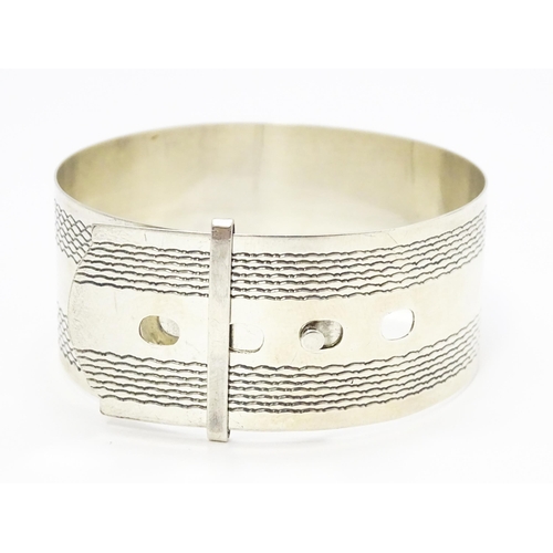 765 - A silver bangle bracelet formed as a belt with engraved decoration. Marked Sterling Silver.