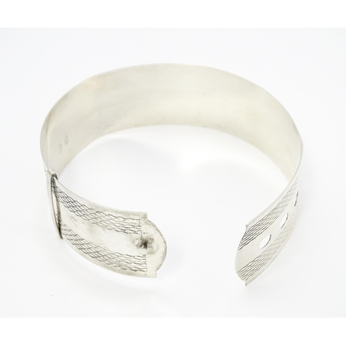 765 - A silver bangle bracelet formed as a belt with engraved decoration. Marked Sterling Silver.