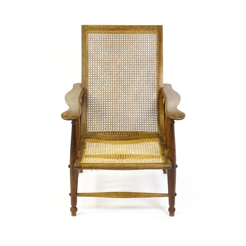 1694 - An Arts & Crafts bergère chair with a caned backrest and seat, the shaped arms supported by turned t... 