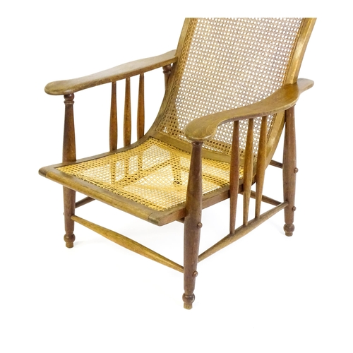 1694 - An Arts & Crafts bergère chair with a caned backrest and seat, the shaped arms supported by turned t... 