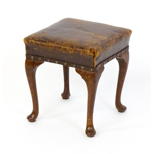 1718 - A late 19thC / early 20thC oak footstool with a leather upholstered stool and raised on four cabriol... 