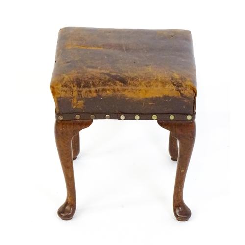 1718 - A late 19thC / early 20thC oak footstool with a leather upholstered stool and raised on four cabriol... 