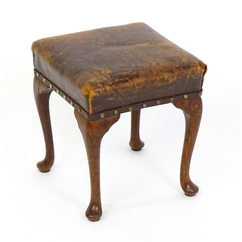 1718 - A late 19thC / early 20thC oak footstool with a leather upholstered stool and raised on four cabriol... 