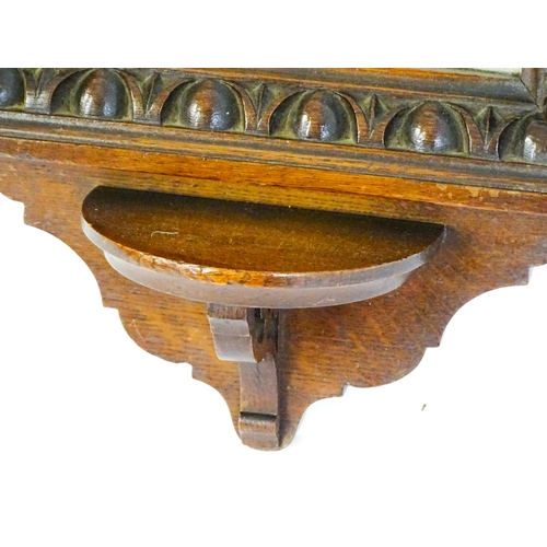 1724 - An Edwardian oak shield shaped mirror with carved egg and dart detailing and a small display shelf. ... 