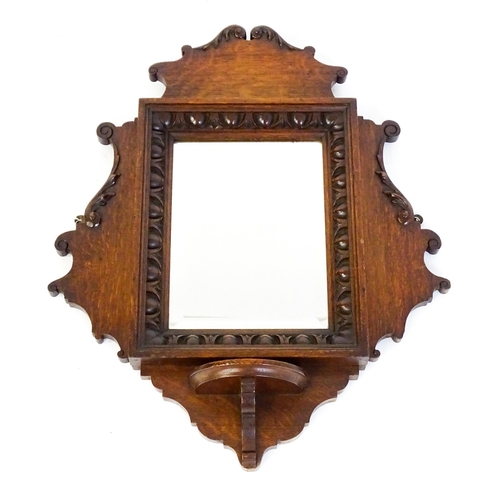 1724 - An Edwardian oak shield shaped mirror with carved egg and dart detailing and a small display shelf. ... 