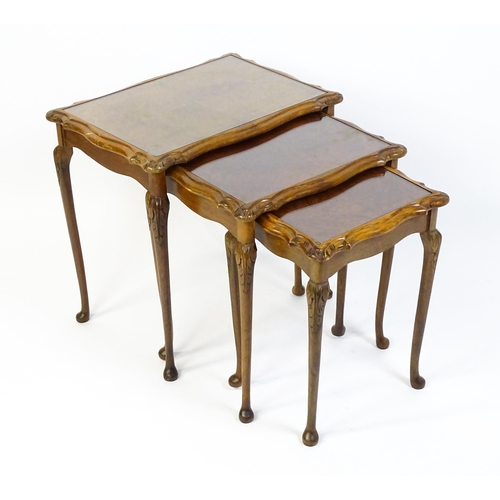 1599 - A mid / late 20thC nest of three burr walnut topped tables raised on acanthus carved legs terminatin... 